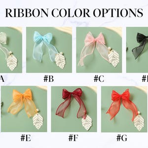 May include: Ribbon color options are displayed, showcasing seven different sheer ribbon bows. Each bow is paired with a leaf-shaped charm and a pearl. The bows come in various colors, including white, blue, pink, black, orange, burgundy, and red.