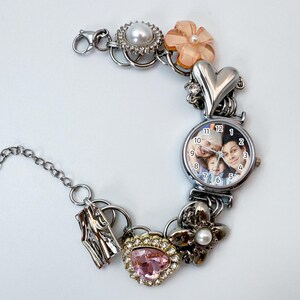 Puede incluir: Pulsera de abalorios plateada con una esfera de reloj que muestra una foto familiar. La pulsera incluye varios abalorios: un coraz&oacute;n, flores, una gema rosa y una perla. La esfera del reloj muestra la hora con n&uacute;meros negros.