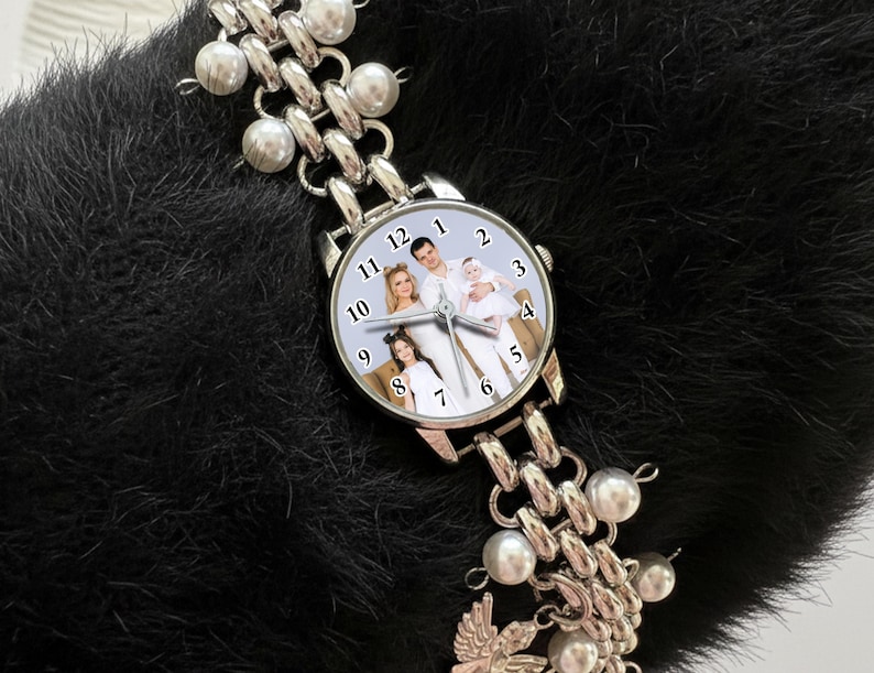 May include: Silver-toned wristwatch with a family photo on the watch face. The watch has a chain-link band with pearl accents. The watch is displayed on a black, textured surface.