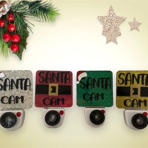 May include: Four different colored night lights with a Santa Cam design. The night lights are silver, red, green, and gold. Each night light has a small white light bulb.
