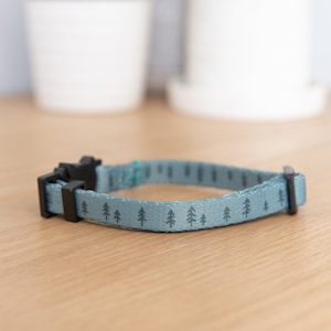 May include: A light blue dog collar with a black buckle and a repeating pattern of small green trees.