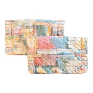 May include: Two rectangular quilted pillow shams featuring a multi-colored abstract pattern with blocks of muted teal, soft peach, dusty rose, and cream. The fabric displays a textured, stitched grid design across the entire surface of both items.