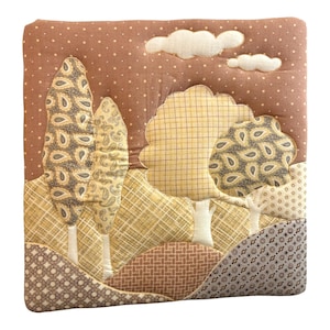 May include: A square fabric wall hanging featuring a quilted landscape scene. The design includes tall trees with paisley patterns, rounded trees with yellow plaid, and rolling hills in various brown and cream geometric prints under white clouds.