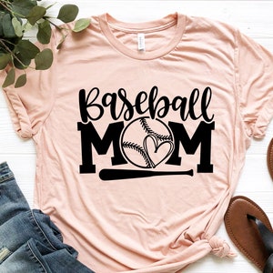 Op de afbeelding: Een roze T-shirt met de tekst "Baseball Mom" in zwarte letters. Een baseball met een hart erin is gecentreerd tussen de woorden "Mom". Een zwarte honkbalknuppel bevindt zich onder de baseball.