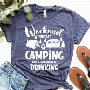May include: A navy blue t-shirt with white text that reads "Weekend Forecast Camping with a good chance of Drinking". The shirt features a white illustration of a tent, a campfire, a camper, and a beer bottle.