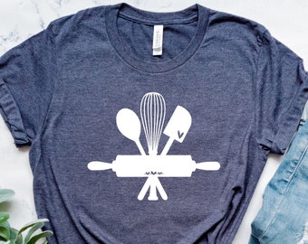May include: A dark heather gray t-shirt with a white graphic of a rolling pin, a whisk, a spoon, and a spatula. The graphic is centered on the shirt.