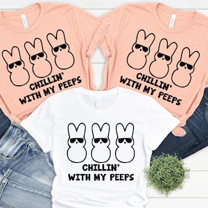Peut inclure: Trois t-shirts de couleur p&ecirc;che avec un motif noir de trois Peeps de dessin anim&eacute; portant des lunettes de soleil et le texte "Chillin' with my peeps".