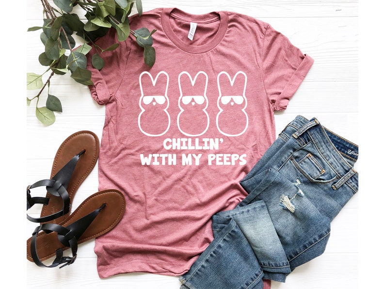Peut inclure: Un t-shirt rose avec un motif blanc de trois Peeps de P&acirc;ques portant des lunettes de soleil. Le texte "Chillin' with my peeps" est imprim&eacute; sous les Peeps.