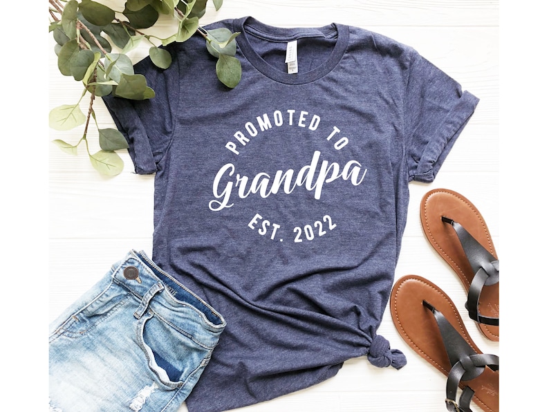 May include: A navy blue t-shirt with white text that reads "Promoted to Grandpa Est. 2022".