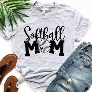 Puede incluir: Una camiseta gris con el texto "Softball Mom" en letras negras y un gr&aacute;fico de softball negro con un peque&ntilde;o coraz&oacute;n.