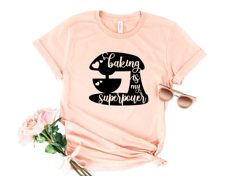 May include: A peach-colored t-shirt with a black graphic of a stand mixer and the text "Baking is my superpower".