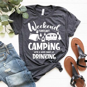 May include: A dark gray t-shirt with a white graphic that says "Weekend Forecast Camping with a good chance of Drinking". The graphic also includes a tent, a campfire, and a camper.