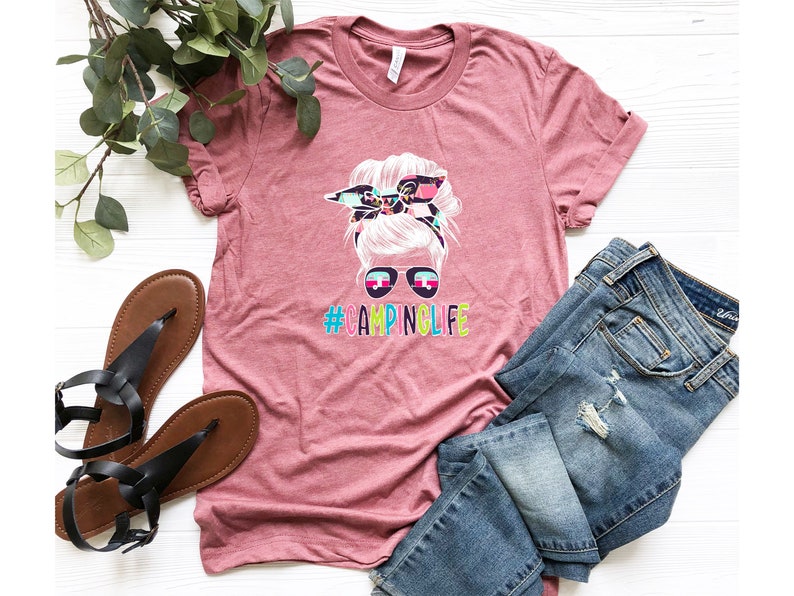 May include: A pink t-shirt with a graphic of a woman with a messy bun and sunglasses. The text "#CAMPINGLIFE" is printed below the graphic.