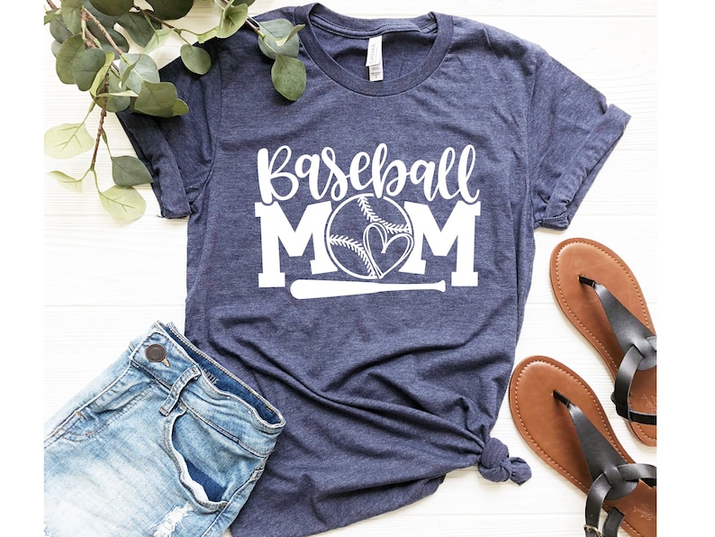 Op de afbeelding: Een marineblauw t-shirt met de tekst "Baseball Mom" in wit, met een honkbal met harten en een honkbalknuppel.