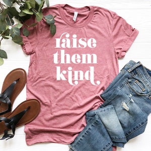 May include: A pink t-shirt with the text "raise them kind" in white lettering.