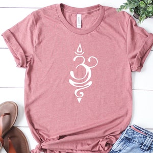 May include: A mauve colored t-shirt with a white Om symbol graphic. The shirt is made of a soft, comfortable material.