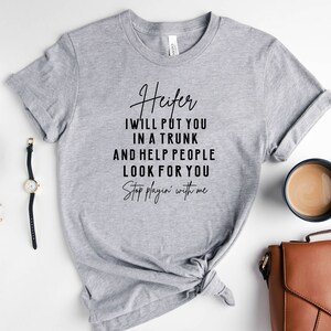May include: A gray t-shirt with the text "Heifer I will put you in a trunk and help people look for you Stop playin' with me" printed in black.