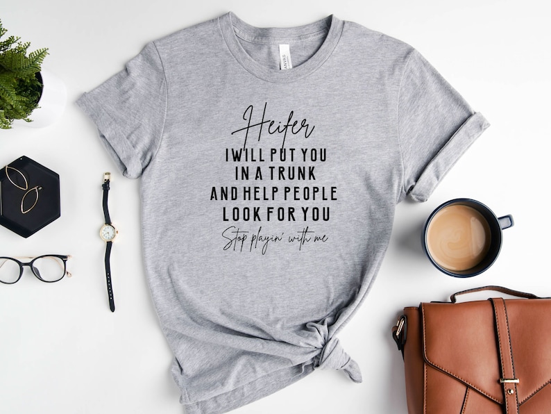 May include: A gray t-shirt with the text "Heifer I will put you in a trunk and help people look for you Stop playin' with me" printed in black.