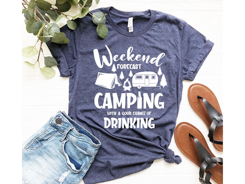 May include: A navy blue t-shirt with white text that reads "Weekend Forecast Camping with a good chance of Drinking". The shirt features a white illustration of a tent, a campfire, a camper, and a beer bottle.