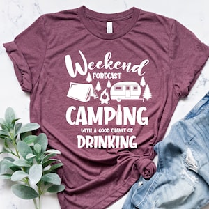 May include: A maroon t-shirt with white text that reads "Weekend Forecast Camping with a good chance of drinking". The shirt features a white silhouette of a tent, campfire, camper, and beer bottle.