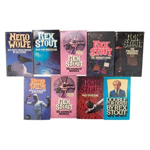 May include: A collection of vintage paperback books by Rex Stout and Nero Wolfe. The book covers feature various colors, including blue, pink, and red, with illustrations of a pigeon, a revolver, and a man. Titles include "The Sound of Murder" and "Double for Death."