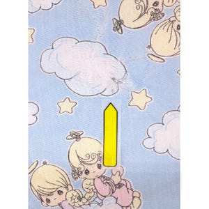 May include: Pale blue fabric featuring a repeating pattern of cartoon angels, clouds, and stars. The angels have blonde hair and wear pink and white clothing. The clouds and stars are yellow. The fabric has a quilted texture.