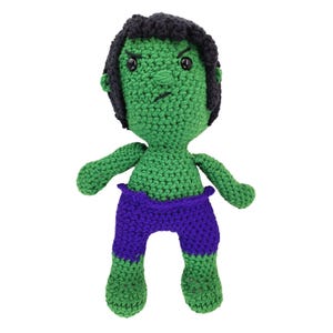 May include: A handmade green crochet doll resembling the Hulk character. The doll has black hair, a stern expression, and is wearing purple shorts. The doll is approximately 8 inches tall and is made of yarn.