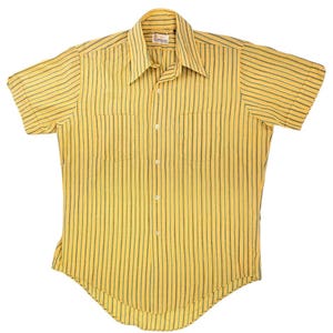 Puede incluir: Una camisa de manga corta con botones en tono amarillo con rayas verticales de color verde oscuro. La camisa presenta un cuello puntiagudo, una tapeta frontal con botones blancos y dos bolsillos en el pecho. El dobladillo es curvo.