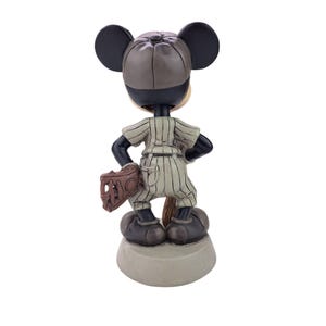 Peut inclure: Figurine de Mickey Mouse en uniforme de baseball, vue de dos. La figurine porte une chemise &agrave; rayures, une casquette de baseball et tient un gant. Le socle est de couleur gris clair.