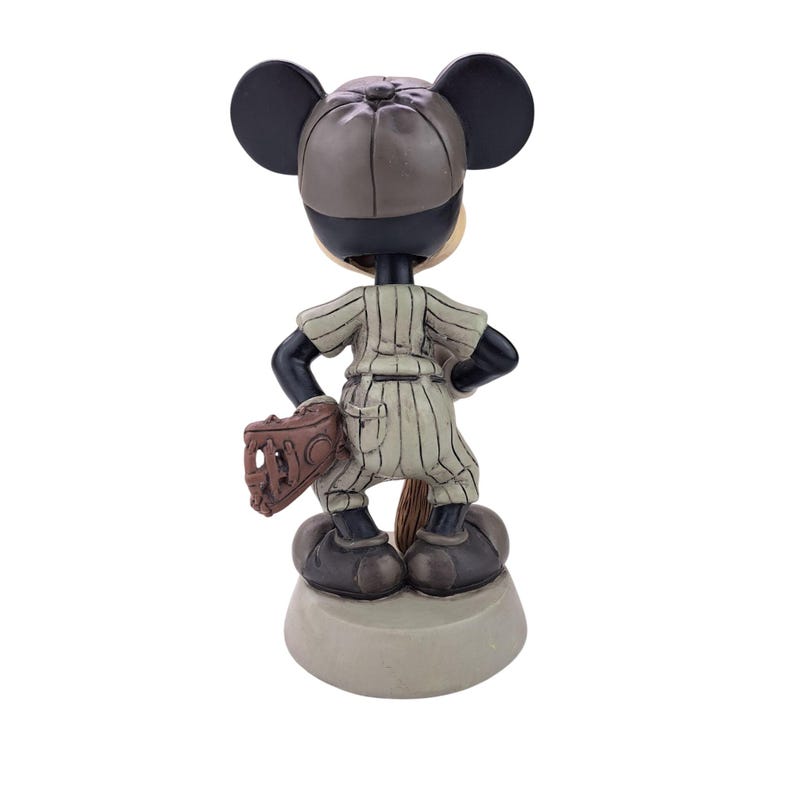 Peut inclure: Figurine de Mickey Mouse en uniforme de baseball, vue de dos. La figurine porte une chemise &agrave; rayures, une casquette de baseball et tient un gant. Le socle est de couleur gris clair.