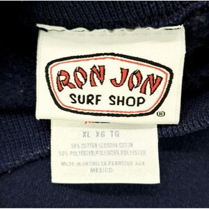 May include: Close-up of a navy blue garment tag. The tag features the red and white "RON JON SURF SHOP" logo. Below the logo are size indicators and fabric content details. The tag reads "MADE IN MEXICO".