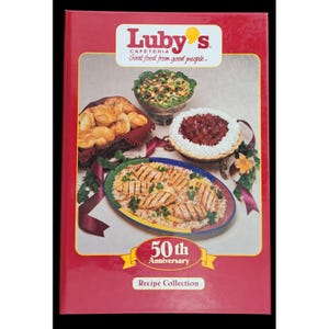 Könnte beinhalten: Ein rotes Kochbuch mit dem Titel "Luby's Cafeteria Recipe Collection" mit einem Banner zum 50. Jahrestag. Das Cover zeigt Bilder von verschiedenen Gerichten, darunter Brot, Salat, gegrilltes Hähnchen und einen Kuchen.