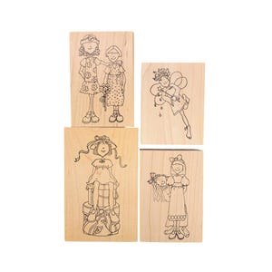 May include: Set of four wooden stamps featuring whimsical illustrations of girls. The stamps depict girls in dresses, one with a bouquet, another as a fairy, and two others with hats and bows. The designs are in black ink.
