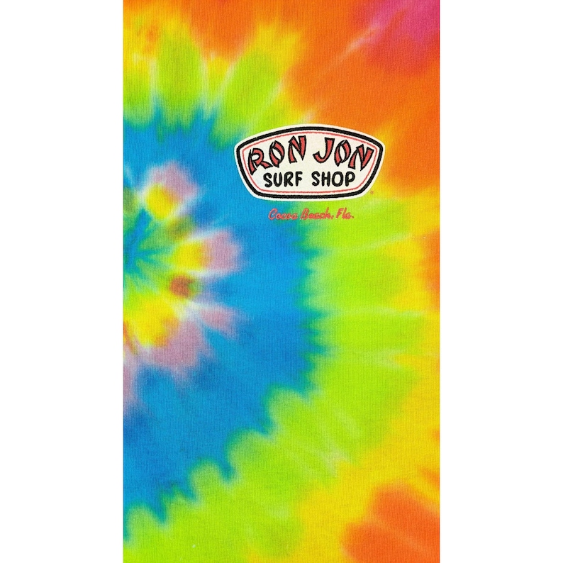 Puede incluir: Una toalla de playa te&ntilde;ida con un remolino de colores vibrantes: naranja, amarillo, verde, azul y morado. La toalla presenta el logotipo "Ron Jon Surf Shop" en un &oacute;valo blanco con borde negro.