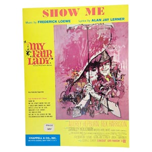 Peut inclure: Partition de la chanson "Show Me" de la comédie musicale "My Fair Lady", avec Audrey Hepburn et Rex Harrison. La couverture est jaune avec le titre en rouge et une illustration rose des acteurs sous un parapluie.
