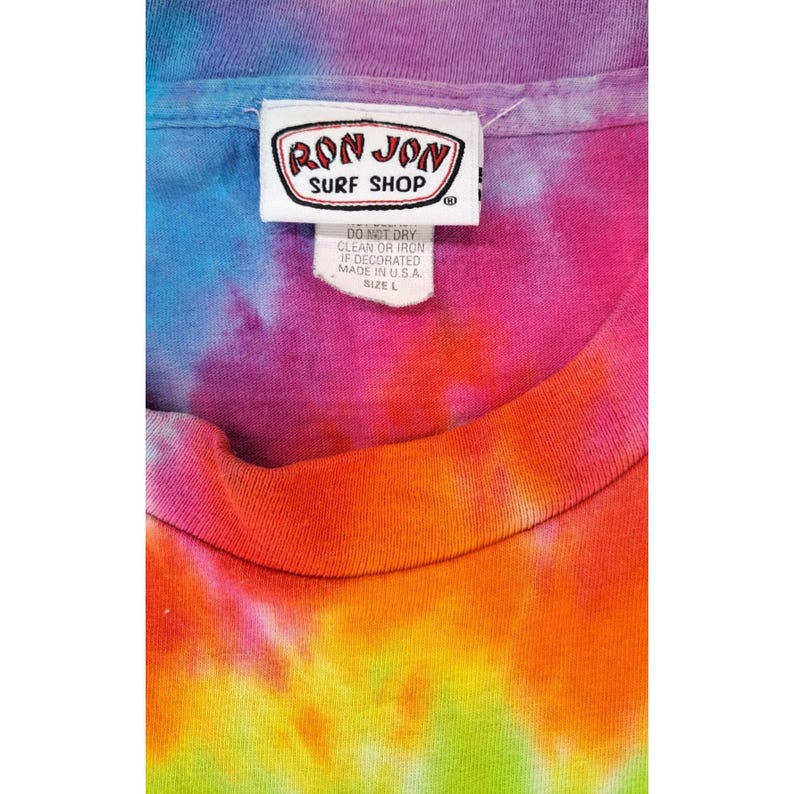 Puede incluir: Una camiseta te&ntilde;ida con un vibrante conjunto de colores, incluyendo azul, morado, naranja y verde. La camiseta tiene una etiqueta con el texto "RON JON SURF SHOP" e instrucciones de lavado. Talla L.