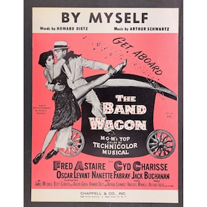 Könnte beinhalten: Vintage Notenblatt-Cover für "By Myself" und das Musical "The Band Wagon". Das Cover zeigt ein tanzendes Paar vor einem stilisierten Wagen, mit den Namen Fred Astaire und Cyd Charisse. Der Hintergrund ist rosa und schwarz.