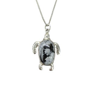 Può includere: Una collana con pendente a forma di tartaruga argentata. Il pendente presenta una pietra nera e bianca incastonata in una cornice a forma di tartaruga. La collana ha una catena delicata e una chiusura a moschettone.