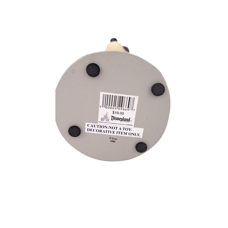 Peut inclure: Une base grise et circulaire avec quatre pieds en caoutchouc noirs. Un autocollant Disneyland est appos&eacute; sur la base, avec le texte "CAUTION: NOT A TOY - DECORATIVE ITEM ONLY." La base supporte une figurine.