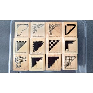 May include: A set of twelve wooden stamps with various corner designs. Each stamp has a black ink design and is mounted on a wooden block. The stamps are in a clear plastic container. The text "©1998 STAMPIN' UP!" is visible on some stamps.