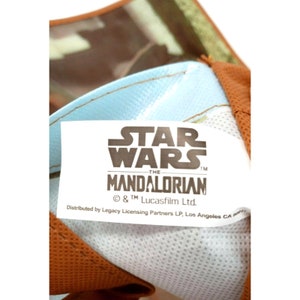 Op de afbeelding: Wit etiket met zwarte tekst die "STAR WARS -THE MANDALORIAN &copy; & TM Lucasfilm Ltd. Distributed by Legacy Licensing Partners LP, Los Angeles CA" luidt.