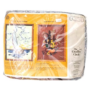 Puede incluir: Un kit de manualidades vintage en un paquete de plástico. El kit presenta dos diseños de bordado enmarcados: "Sunset Sailing" con un velero y "Wooden Duck" con un pato y un arreglo floral. El logotipo de The Creative Circle es visible.