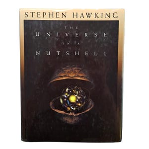 May include: A hardcover book titled "The Universe in a Nutshell" by Stephen Hawking. The cover features a dark background with a detailed illustration of a walnut shell opening to reveal a glowing, spherical representation of the universe.