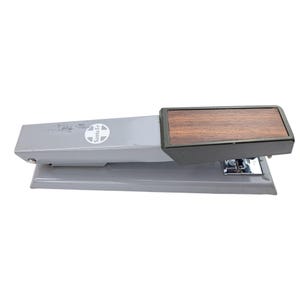 May include: A gray stapler with a wood-grain top. The stapler has the Santa Fe logo printed on the side. The stapler is made of metal and has a chrome staple exit.