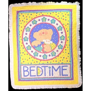 May include: A rectangular quilted blanket with a ruffled white border. The center features a clock face with star-shaped numbers surrounding a bear holding a small toy. The background is yellow with small stars and moons, and the word BEDTIME.