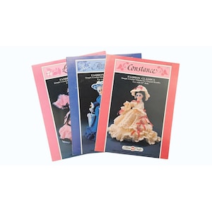 May include: Three vintage crochet pattern books featuring doll designs. The covers are pink, blue, and red, with illustrations of dolls in elegant crochet dresses. Titles include "Fashion Classics" and "Fashion Simple Crochet Stitches."
