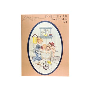 May include: A cross-stitch pattern titled "Potties in Pastels VI" by Alma Lynne. The image features a family scene with a woman and two children in a bathtub, with a dog and toys on the floor. The design is framed in an oval.