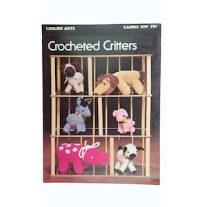 May include: A vintage crochet pattern book titled "Crocheted Critters" featuring various crocheted animal figures. The cover displays a shelf with a collection of crocheted animals, including a lion, donkey, pig, and lamb. The book is from Leisure Arts.