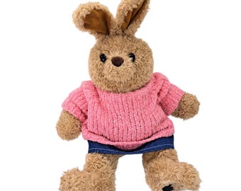 May include: A plush rabbit toy with light brown curly fur, long ears with dark brown inner lining, and black eyes. The rabbit is wearing a textured pink knit sweater and a dark blue denim skirt. The toy has a soft, fuzzy texture throughout.
