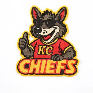 May include: Embroidered patch featuring a cartoon wolf wearing sunglasses and a red shirt with "KC" on it. The wolf gives a thumbs-up, and the word "CHIEFS" is below in yellow letters with a black outline. The patch has a yellow border.